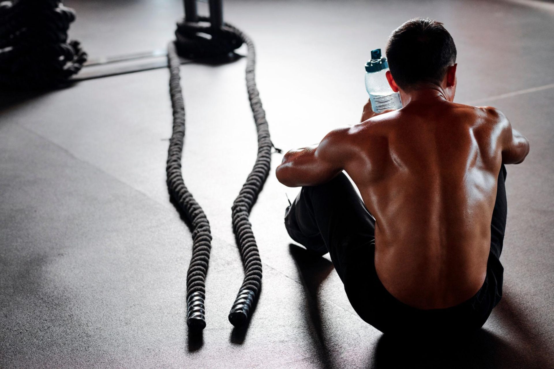 Athlete sitting on gym floor with battle ropes, taking a recovery break between sets