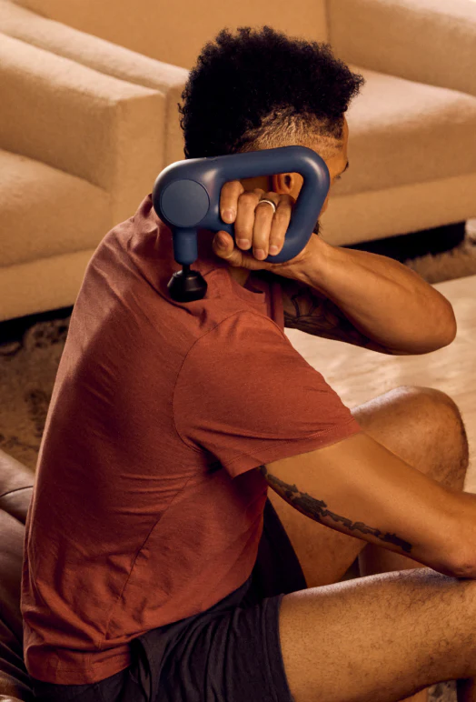 Man using percussion therapy massage gun on shoulder for recovery