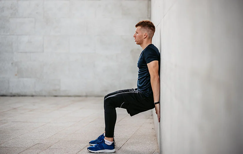 Man performing a wall sit isometric hold for tendon pain relief